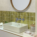 Glossy olive green ceramic square tiles with white grout on bathroom wall